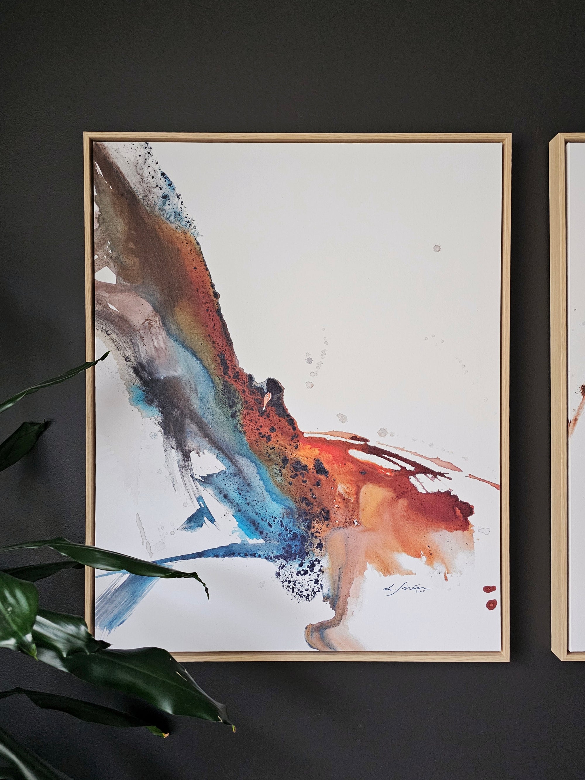 Framed abstract artwork of a Phoenix by Lotta Sirén on a dark wall with a plant in the foreground