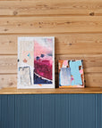 Pink and blue abstract collage paintings by Lotta Sirén on a wooden surface.