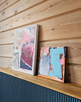 Two abstract paintings by Lotta Sirén on a shelf with wooden wall.