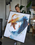 Artist Lotta Sirén holding a large abstract canvas print with splashes of blue, orange, and white in a room.