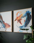 Two abstract art prints by Lotta Sirén on a dark wall with green plants around.