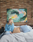 Lotta Sirén sitting on a bed in a room with a colorful green abstract painting on the wall.