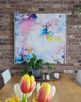 Colorful abstract painting on a brick wall above a dining table with flowers.