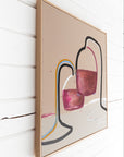 Framed abstract canvas wall art hanging on a white wood-paneled wall. The artwork features abstract shapes in pink, burgundy, black, gray, blue, and yellow on a warm beige background, enclosed in a light natural wood frame by Finnish artist Lotta Sirén