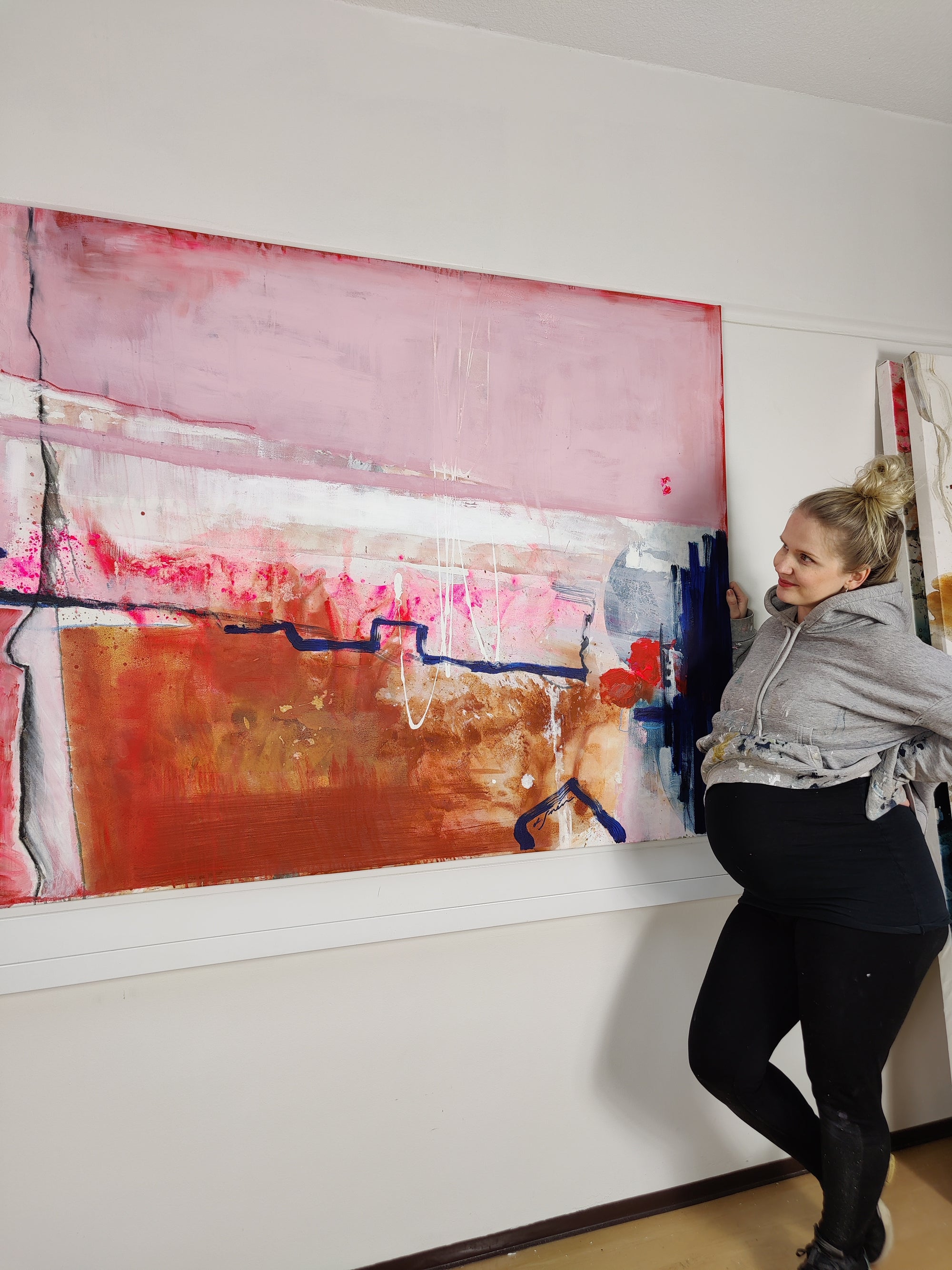 Lotta Sirén standing next to a large abstract painting on a white wall