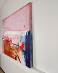 A side profile of an abstract painting with pink, blue, and brown colors on a white wall.