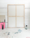 Wooden canvas frame on a white wooden wall with art supplies on a table.