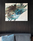 An abstract painting by Finnish Artist Lotta Sirén with black, blue, and gray tones, presented on a wall above a gray sofa with a blue cushion.