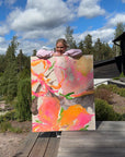 Lotta Sirén holding a colorful semi-abstract floral painting outdoors with trees and sky in the background