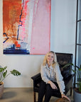 Lotta Sirén sitting on a chair with a dog in a room with large abstract painting on thee wall and plants.