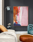 Speed Bump - Limited Edition Canvas Print with oak frame. An abstract canvas print with pink, white and burnt sienna tones and a hint of red & blue. Living room with a colorful abstract painting on the wall, a gray sofa, and a blue armchair.