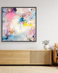 UFO (& other flying vehicles) - Canvas Print. A semi-abstract canvas print with black frame a wall on top of a TV-stand. A light piece with off-white, pastel tones and blue, pink and yellow hues.