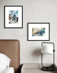 Two framed abstract artworks on a wall above a bed with a lamp.