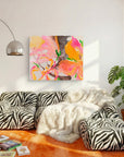 A colorful abstract painting with pink, orange, yellow, and green brushstrokes hangs on a white wall above a modern zebra-print sectional sofa with a white faux-fur throw blanket.