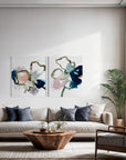 Modern living room with a white sofa, wooden coffee table, and two semi-abstract pieces on a wall.