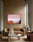 Detours Approved - Limited Edition Canvas Print with black frames on a living room wall above a tv stand. Piece with pink, white and burnt sienna tones and a hint of red & blue. Modern living room with a brown sofa, abstract painting, and decorative items.