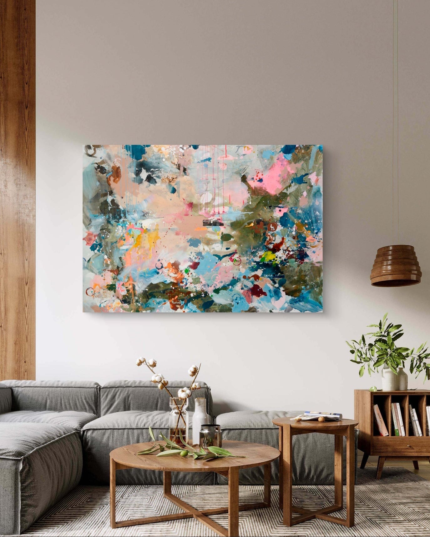 An abstract painting with a colorful paint splatter pattern in shades of blue, pink, beige, and green, displayed in a modern living room setting above a gray sofa.