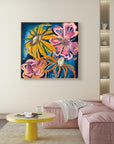 A colorful abstract floral painting with pink, yellow, and orange flowers on a dark blue background, displayed on a beige wall above a pink sofa in a modern living room setting.