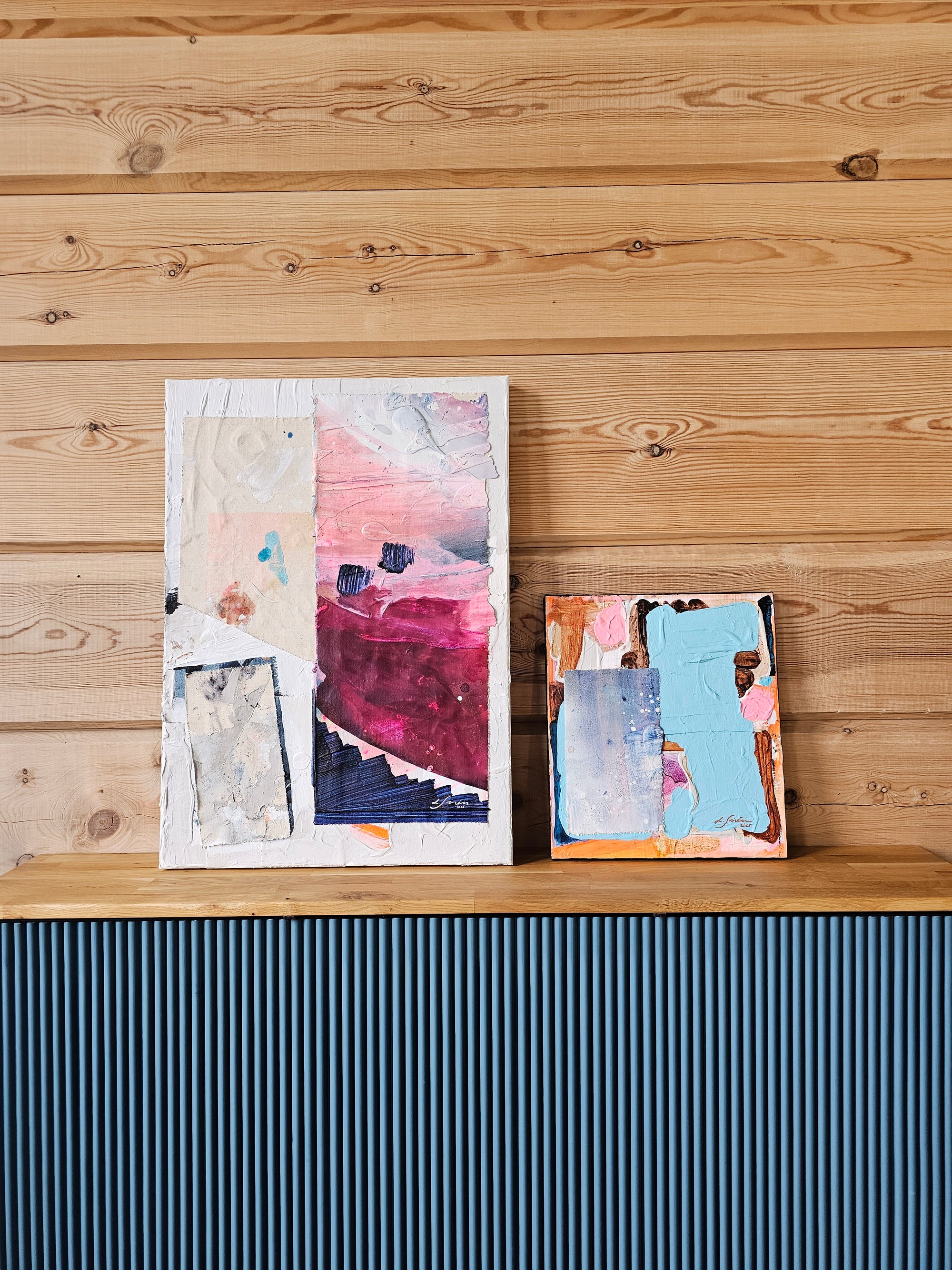 Pink and blue abstract collage paintings by Lotta Sirén on a wooden surface.