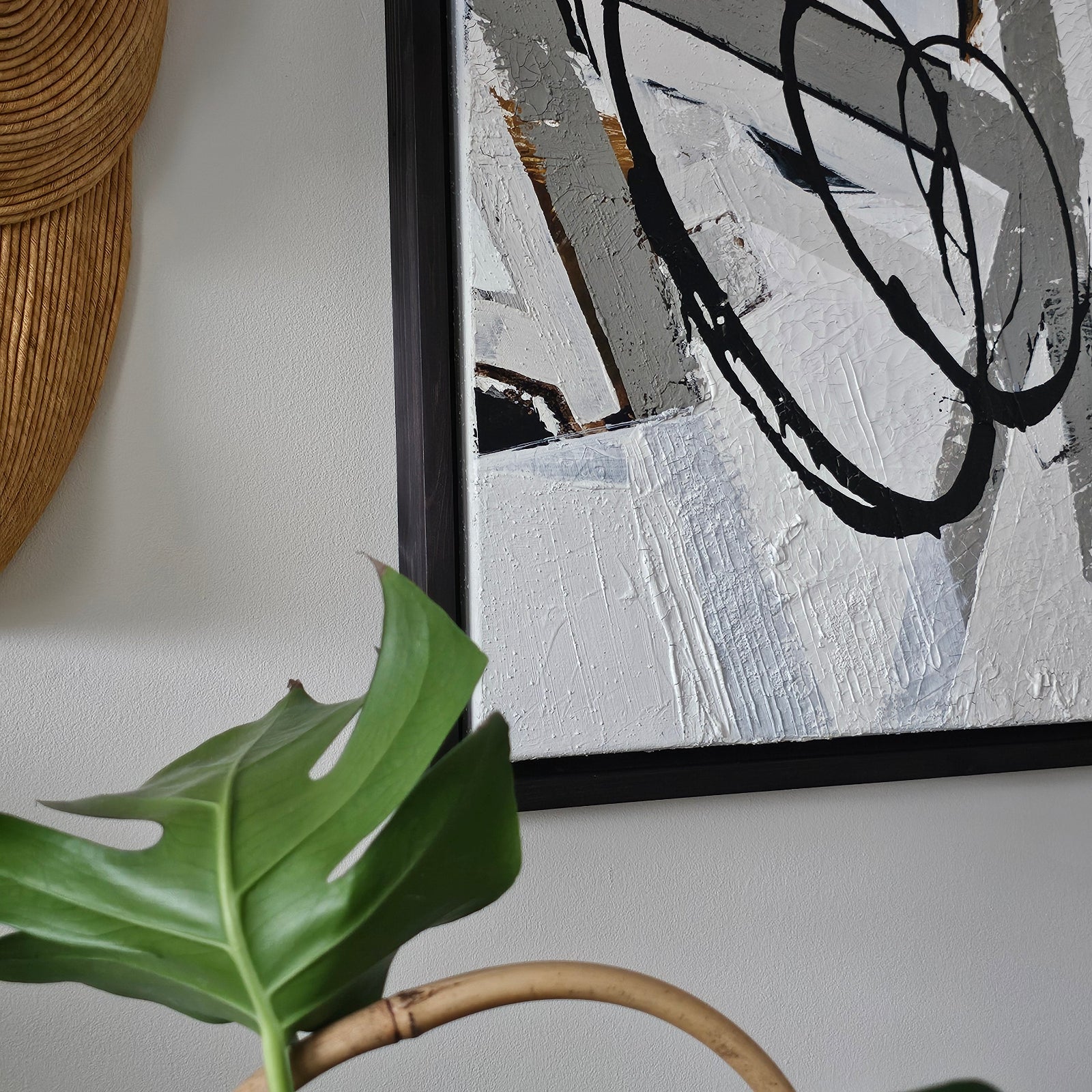 Empowering abstract painting by Lotta Sirén with black and white strokes on a wall, next to a plant and woven basket.