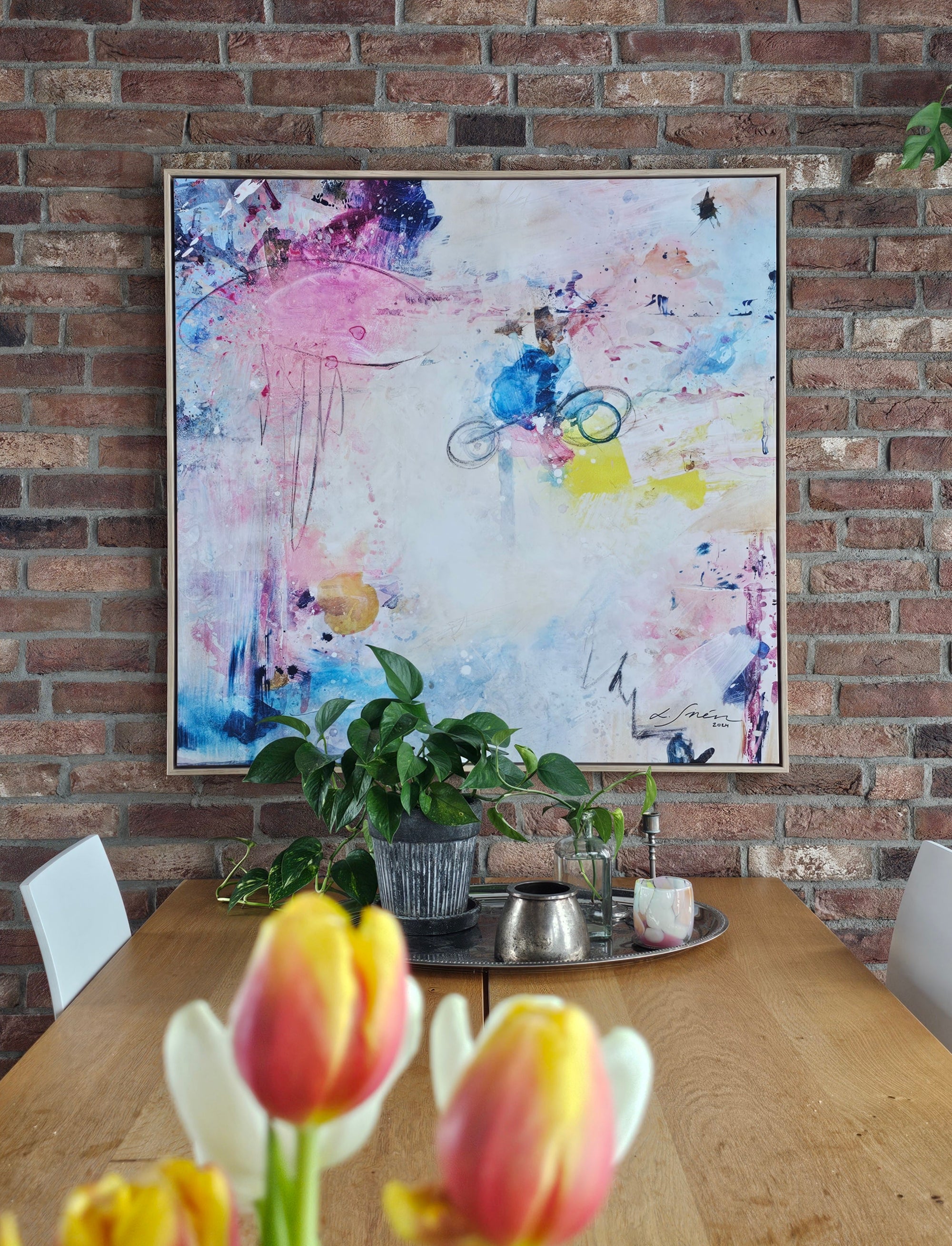 Colorful abstract painting on a brick wall above a dining table with flowers.