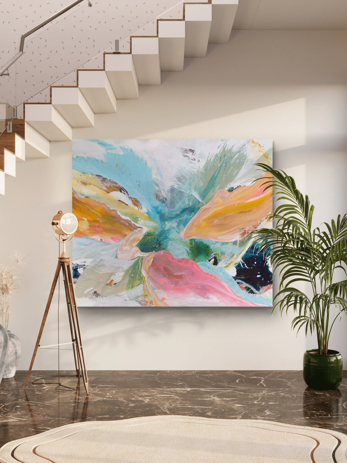 A large abstract canvas painting with vibrant splashes of turquoise, pink, orange, yellow, and green, displayed on a white wall in a modern home interior with a staircase, floor lamp, and potted plant.