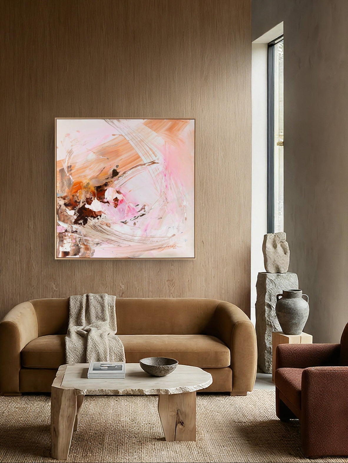 An abstract painting "I Need Space with" pink, peach, and brown brushstrokes hanging on a wooden wall in a modern living room setting with a tan sofa and stone coffee table.