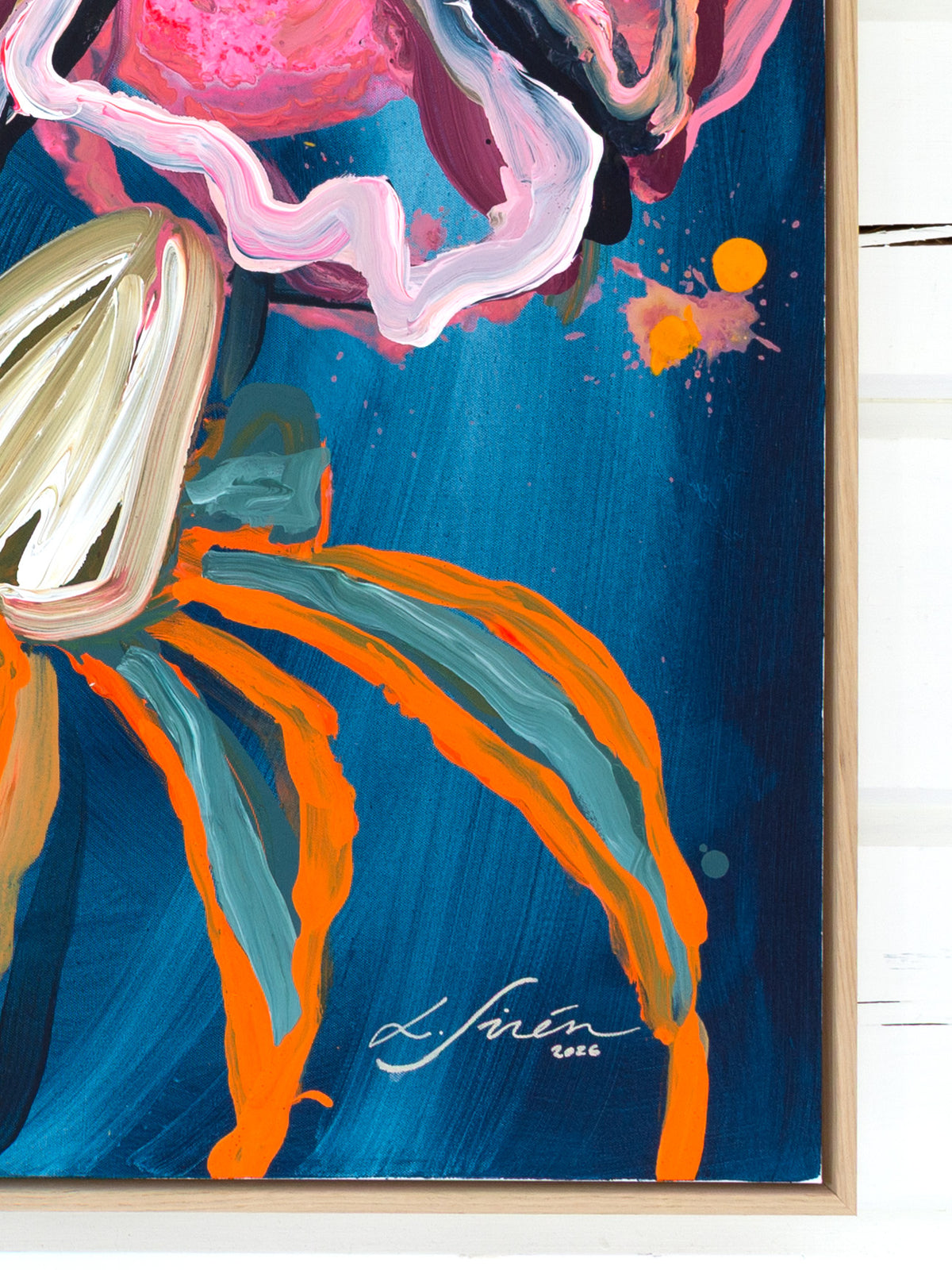 A close-up of a framed abstract painting featuring a dark blue background with bold strokes of orange, teal, pink, white, and black, artist Lotta Sirén signature in the corner. 