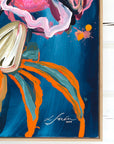 A close-up of a framed abstract painting featuring a dark blue background with bold strokes of orange, teal, pink, white, and black, artist Lotta Sirén signature in the corner. 