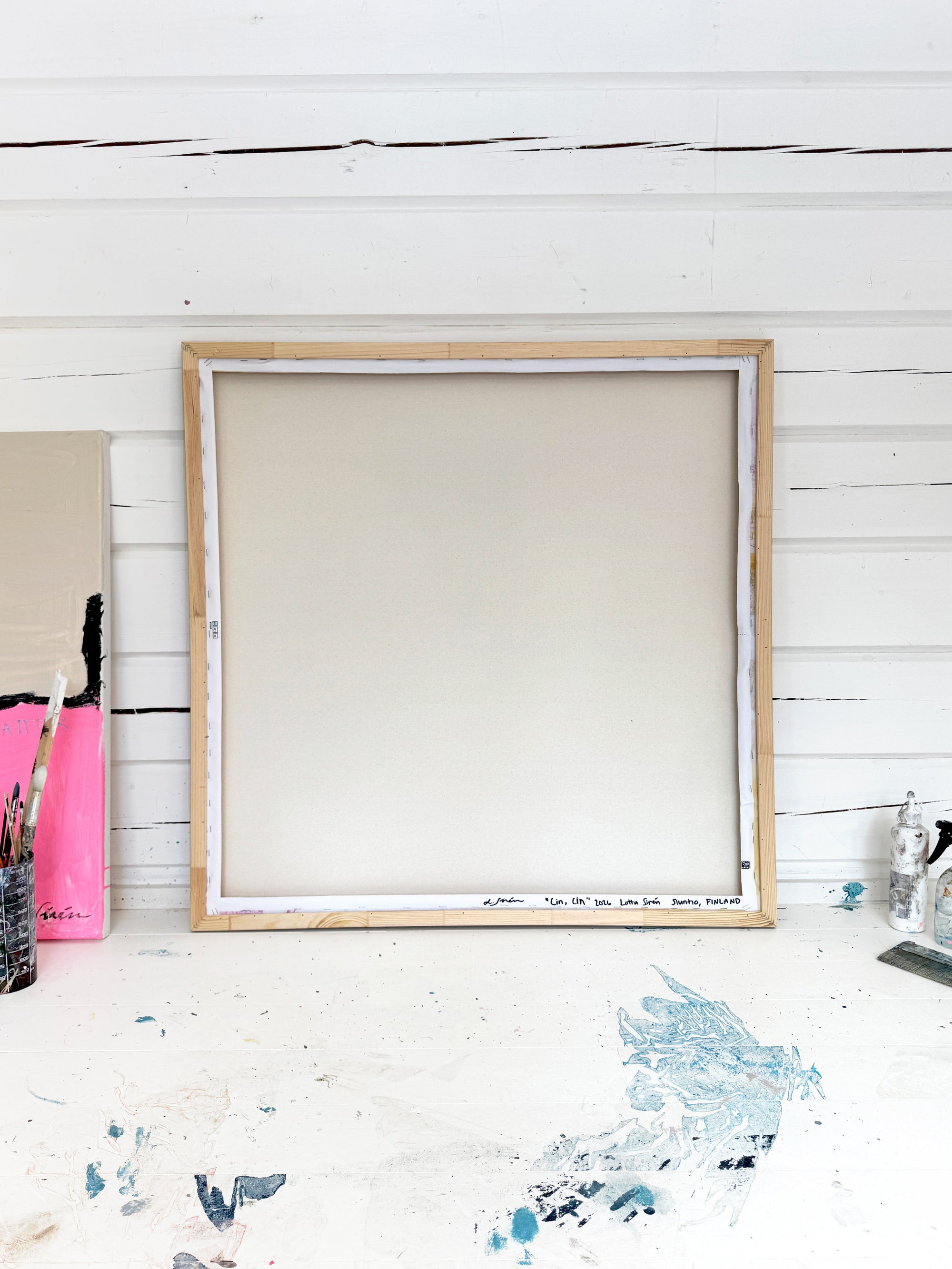 Large wooden frame on a white wooden floor with paint splashes.