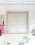 Large wooden frame on a white wooden floor with paint splashes.