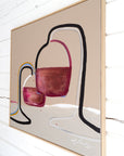A framed abstract painting featuring two wine glasses with burgundy and pink tones, outlined in black and white, hanging on a white wood-paneled wall by Finnish artist Lotta Sirén