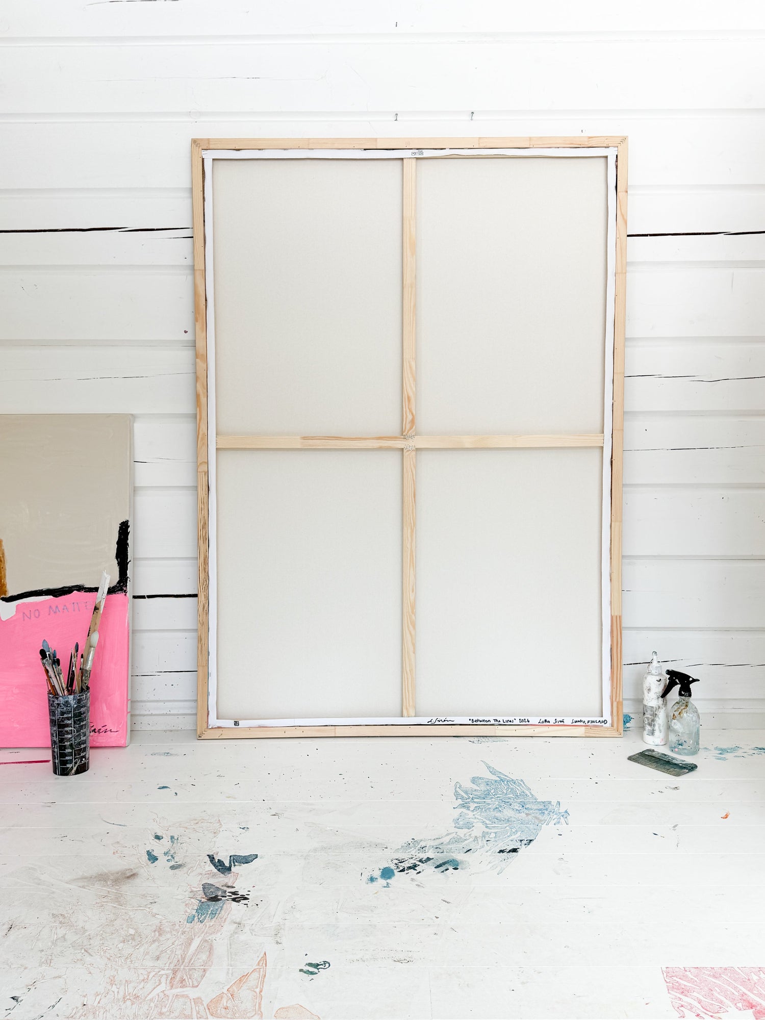 Wooden canvas frame on a white wooden wall with art supplies on a table.