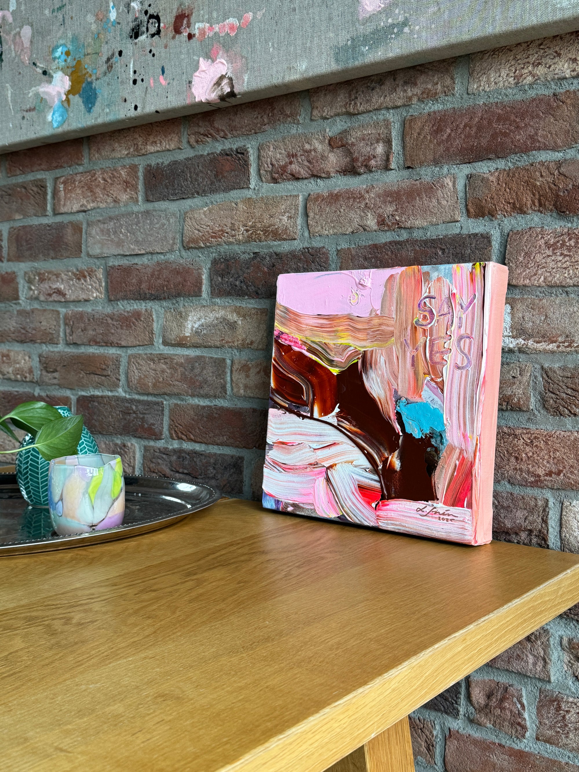 Colorful abstract painting by Lotta Sirén leaning against a brick wall.