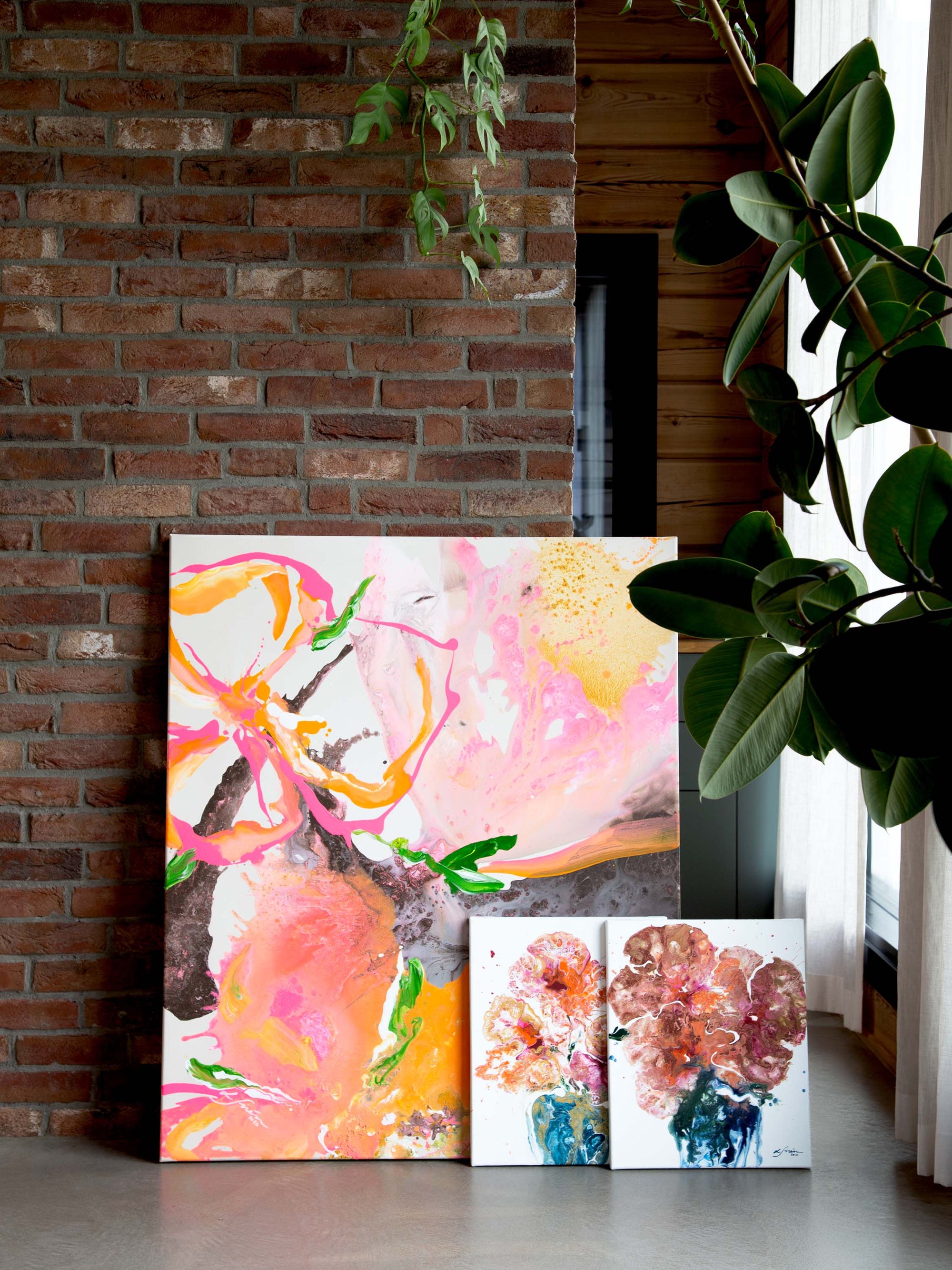 Colorful semi-abstract paintings leaning against a brick wall with a plant in the foreground by Finnish artist Lotta Sirén