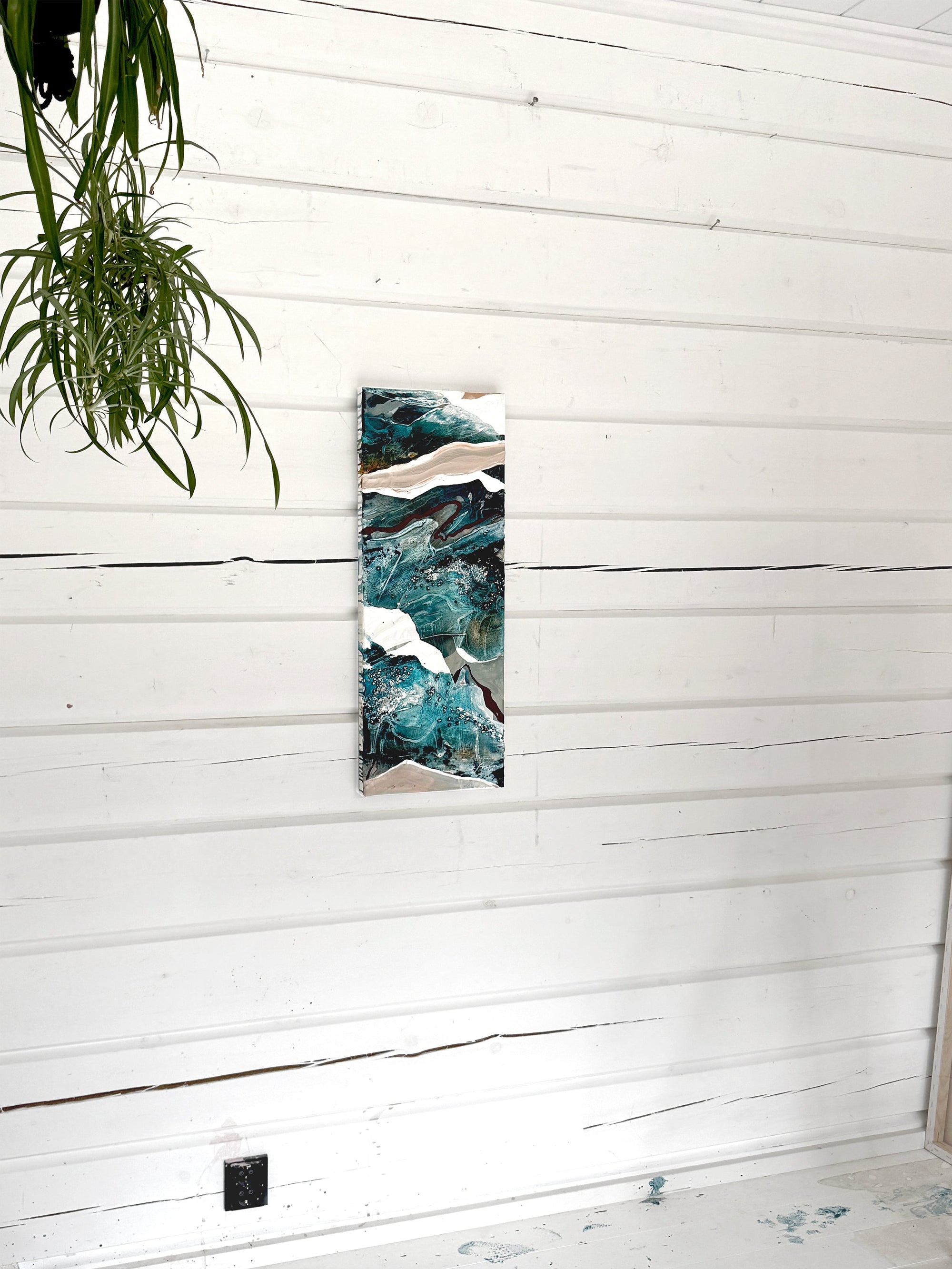 Tall vertical abstract painting on a white wooden wall with a plant by Finnish artist Lotta Sirén