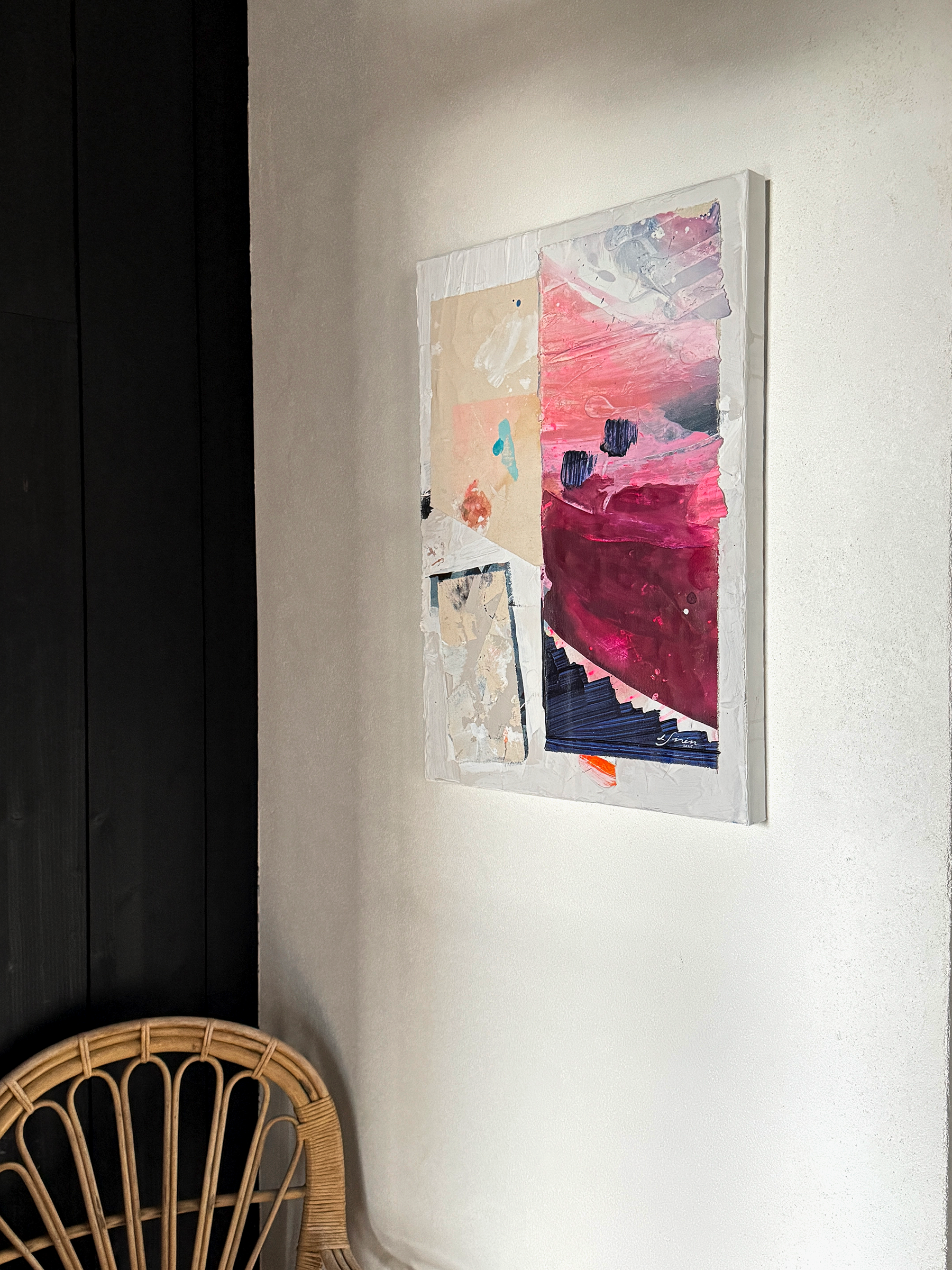 Abstract art piece on a wall next to a wicker chair