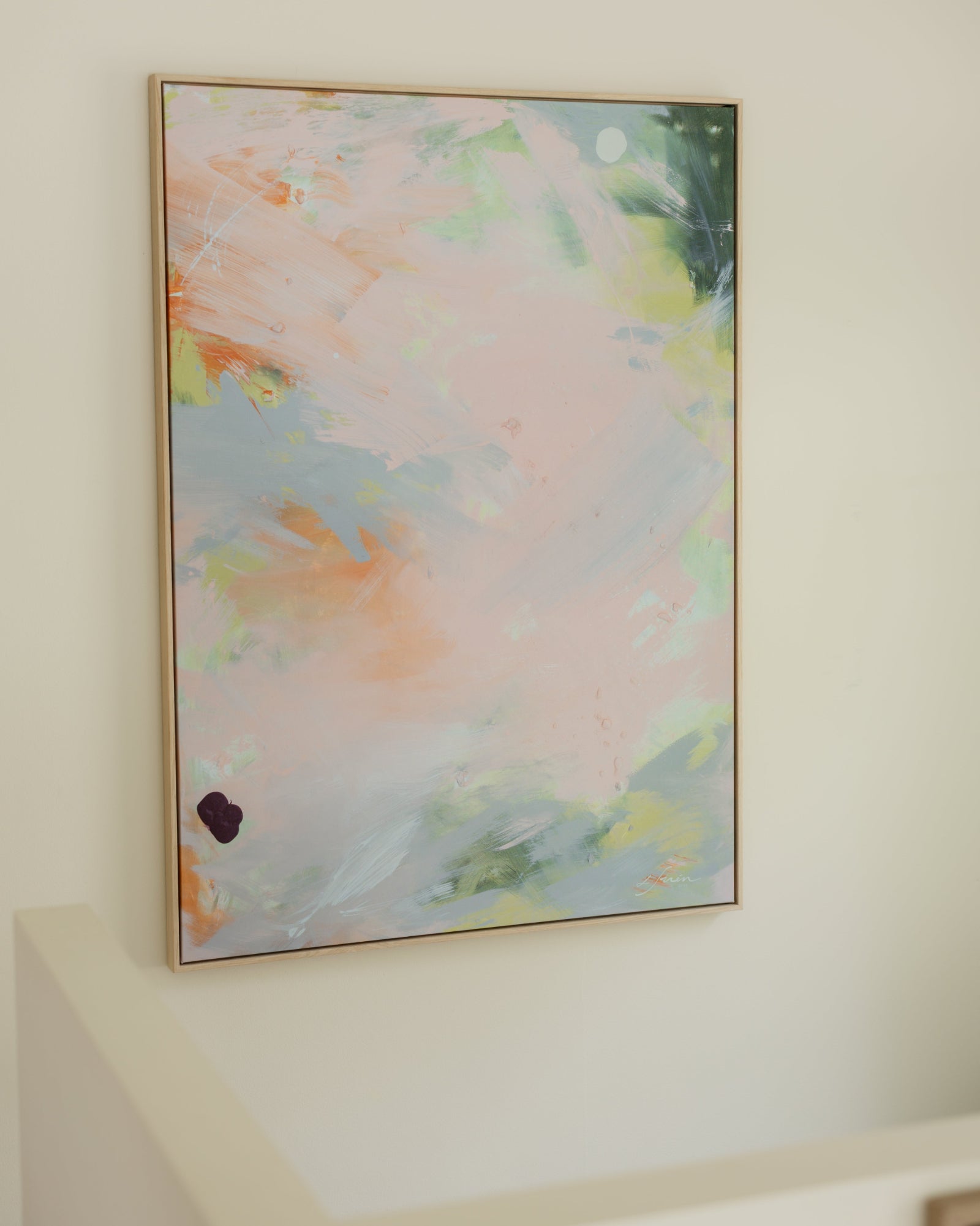 An abstract framed canvas art print with soft pastel brushstrokes in pink, blue, green, and peach, hanging on a warm beige wall.
