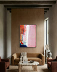 Speed Bump - Limited Edition Canvas Print with black frame. An abstract canvas print with pink, white and burnt sienna tones and a hint of red & blue. Living room with a brown sofa, coffee table, and abstract painting on a wooden wall.