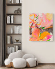 Abstract floral canvas wall art in vibrant pink, orange, and yellow tones, displayed on a light beige wall in a modern living room setting next to a built-in bookshelf and white sofa.