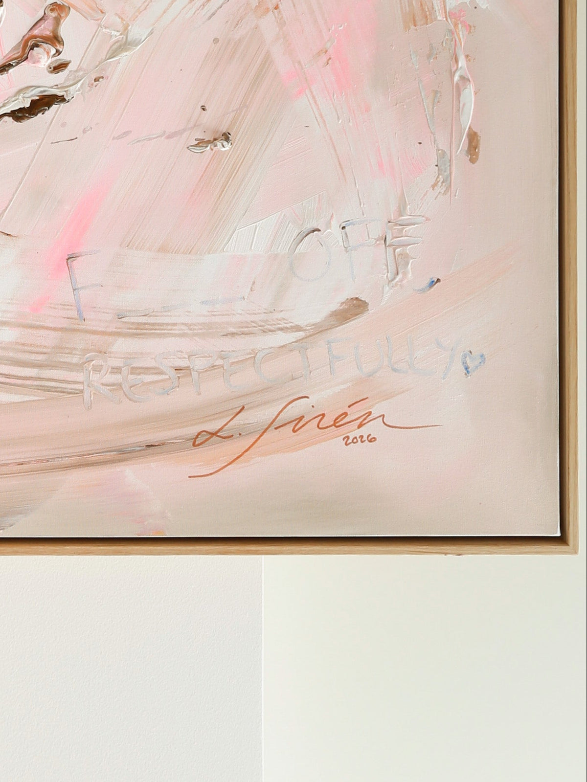 An abstract framed painting featuring soft pink, beige, and white brushstrokes with a signature from artist Lotta Sirén hanging against a white wall.