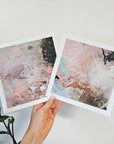 Two abstract art prints held by a hand on a light background